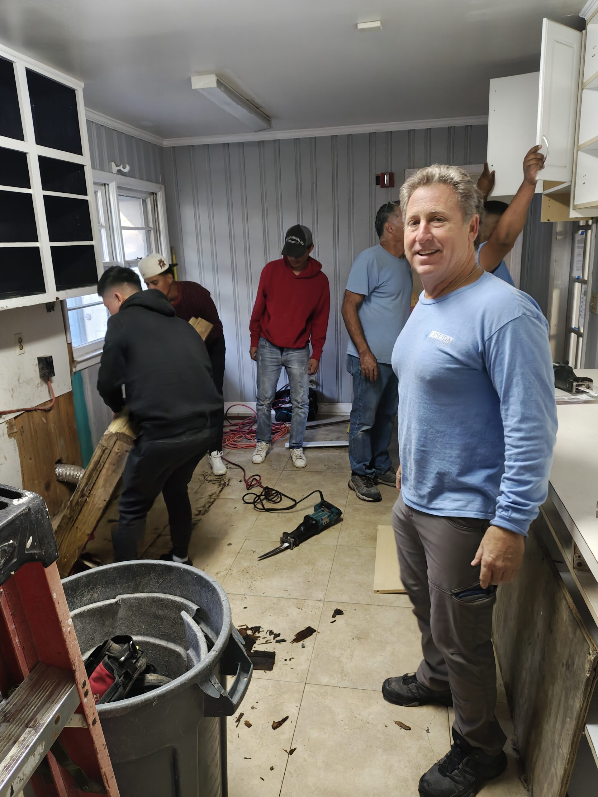 Volunteers working inside the PAWS Atlanta Cat Cottage during demolition, with the old wall covering and subfloor exposed.