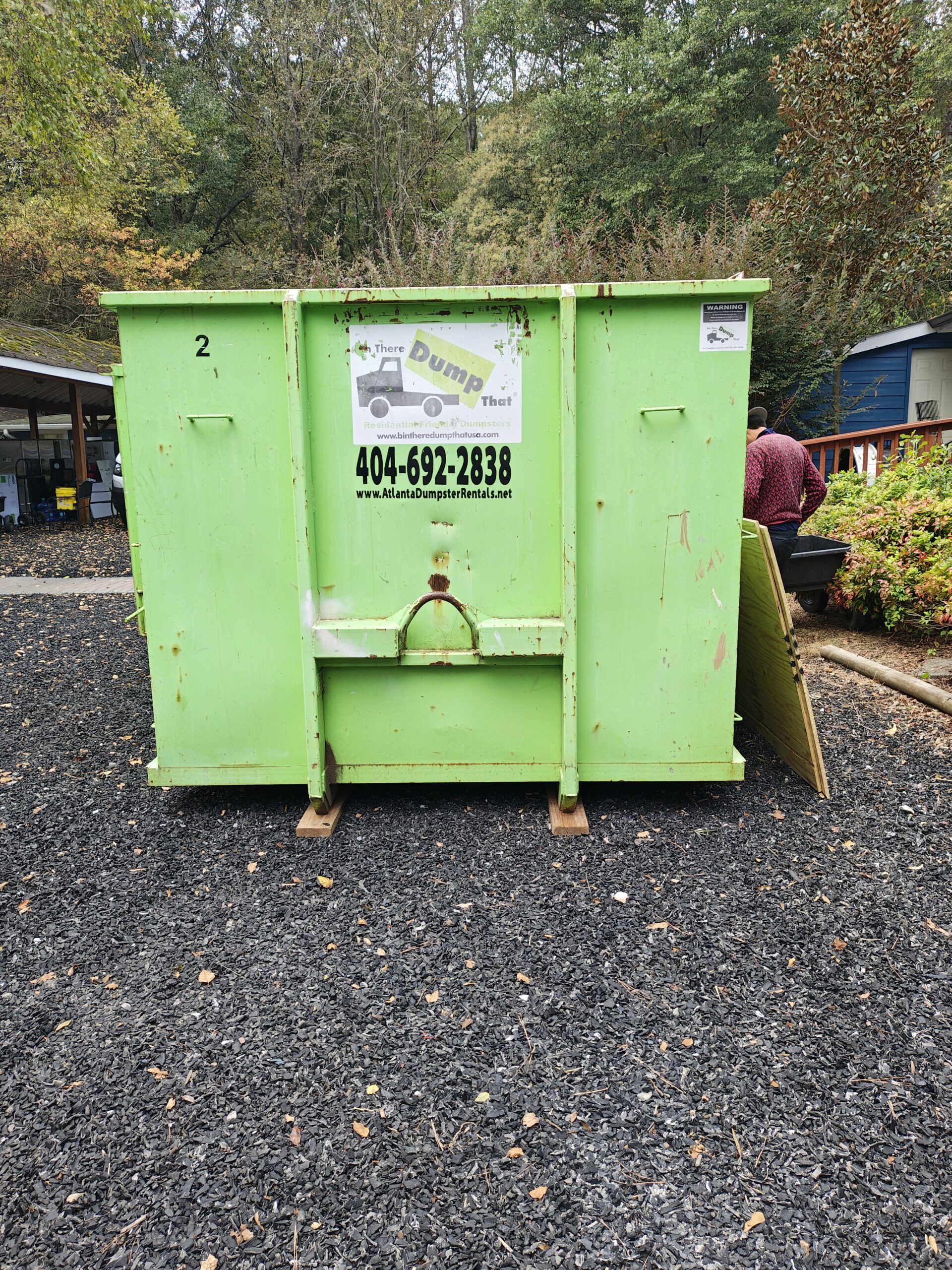 A green Bin There Dump That dumpster parked outside the PAWS Atlanta Cat Cottage while volunteers work behind it.