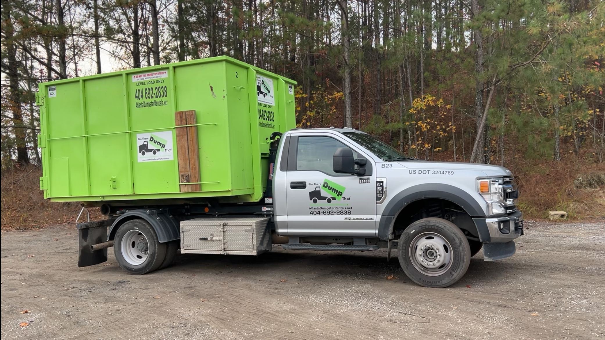 A Bin There Dump That hook lift truck carrying a green roll off dumpster.