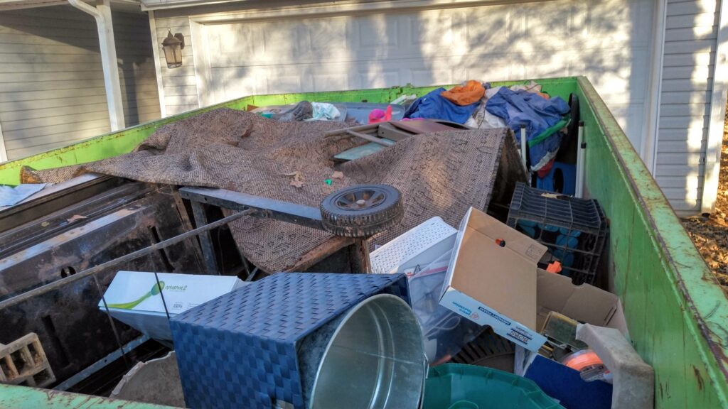Green dumpster full of junk parked in front of a garage during a garage cleanout in Marietta, GA