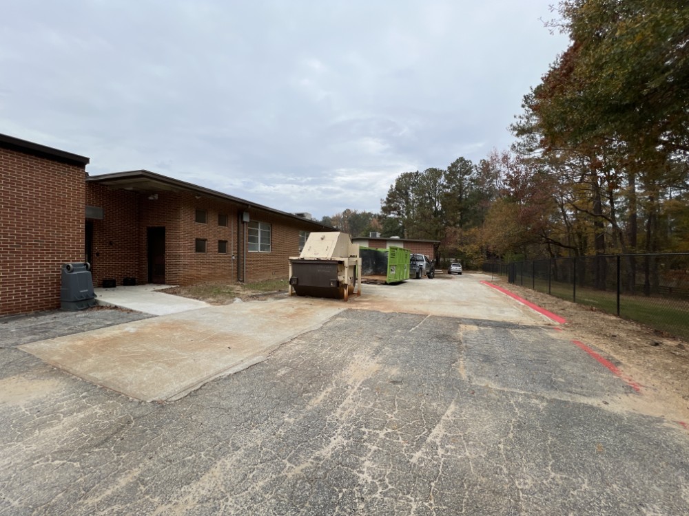 A roll off dumpster positioned on the paved service area behind a brick school building in Mableton, Georgia.