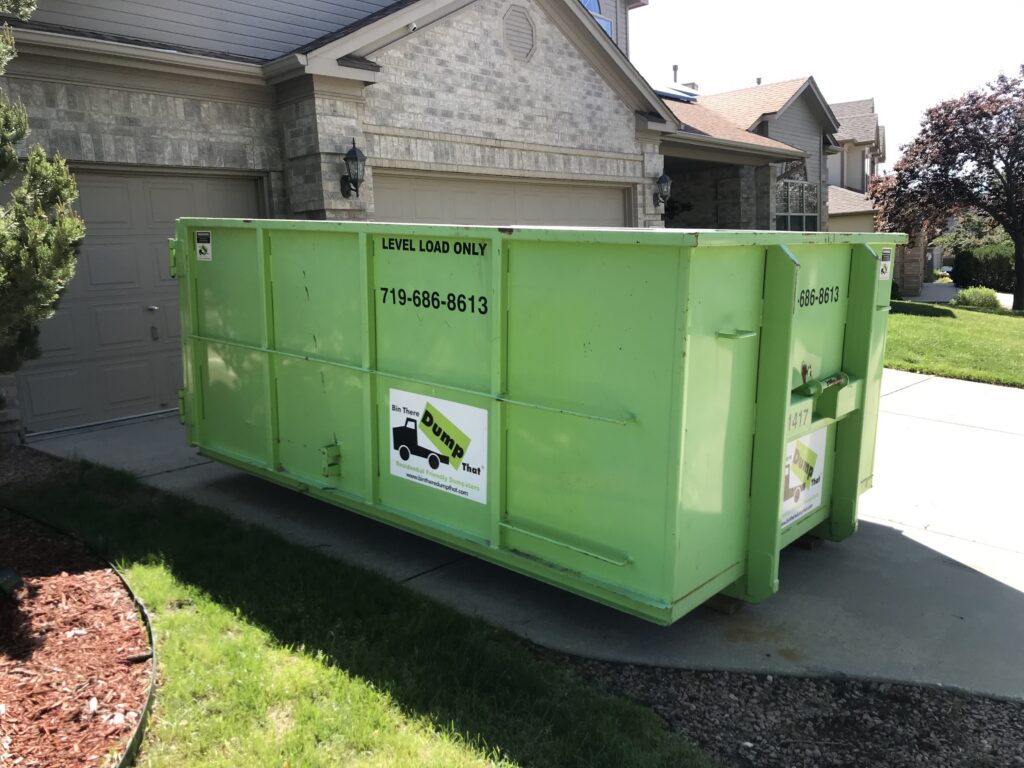 Long dumpster on the wide driveway of a brick and stone two-story home
