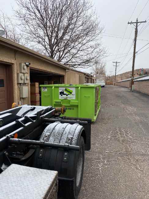 Dumpster placed in an alley behind garages with moving boxes nearby
