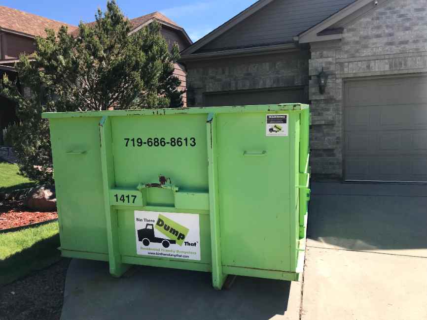 Clean dumpster on the driveway of a brick home with xeriscape landscaping