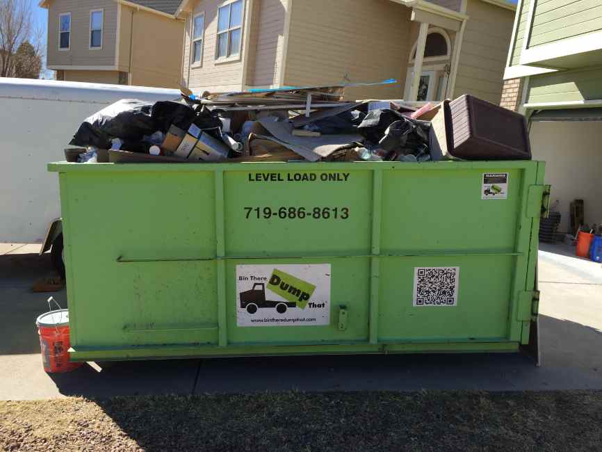 Dumpster loaded to the rail with bags, carpet and household debris
