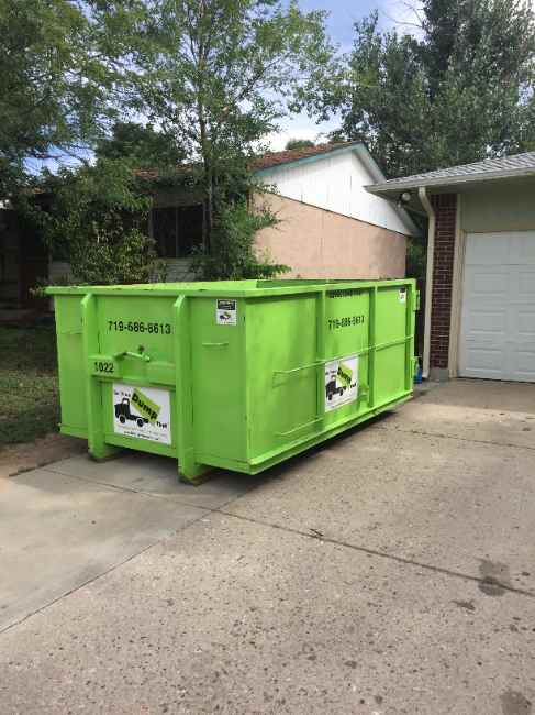 Dumpster on the driveway of an older home with an overgrown yard