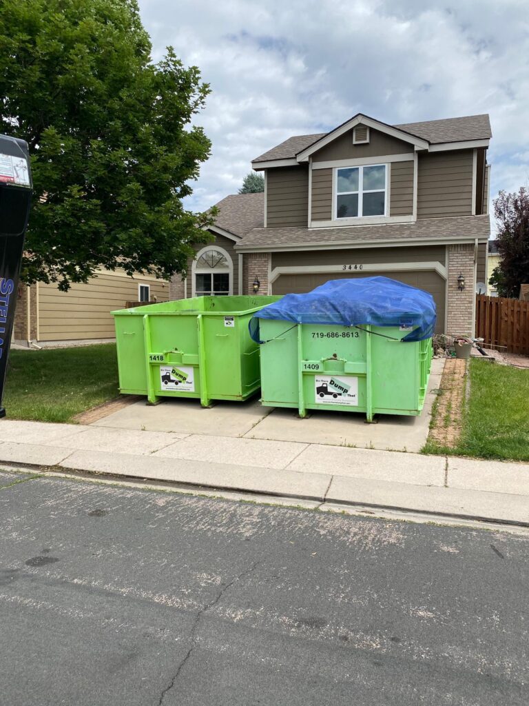 Two dumpsters on a driveway, one covered with a blue tarp