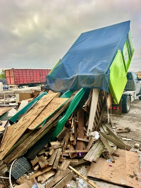 Tarp-covered green dumpster unloading wood and construction debris for a Plainfield, IL dumpster rental service.