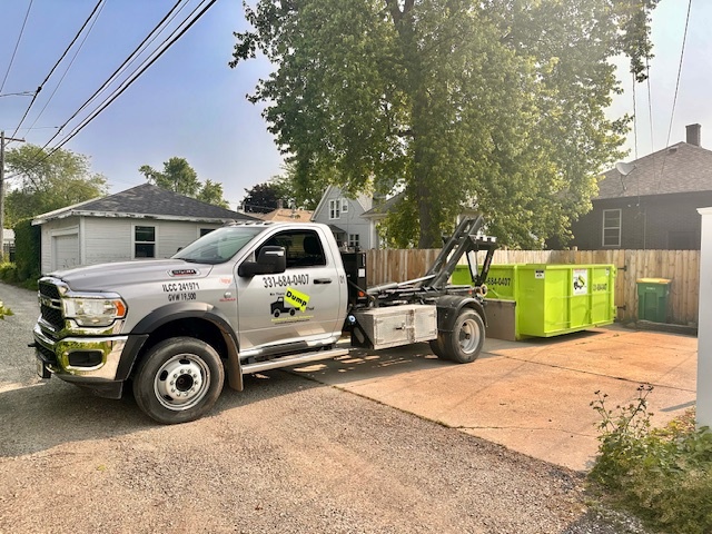 Bin There Dump That truck delivering a green dumpster rental to a residential driveway in Plainfield, IL.